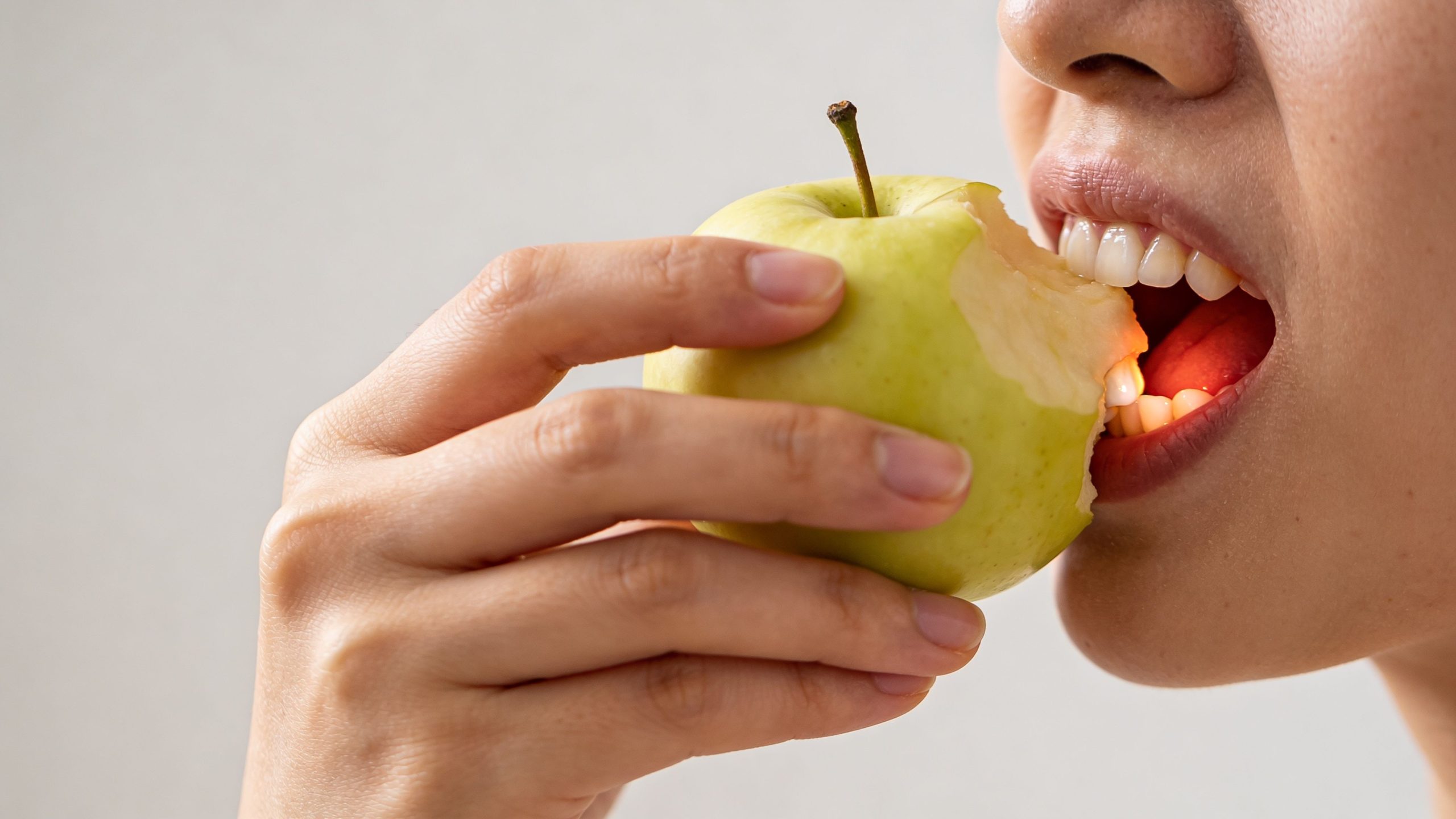 Close-up of a person taking a bite of a fresh green apple showing healthy teeth.