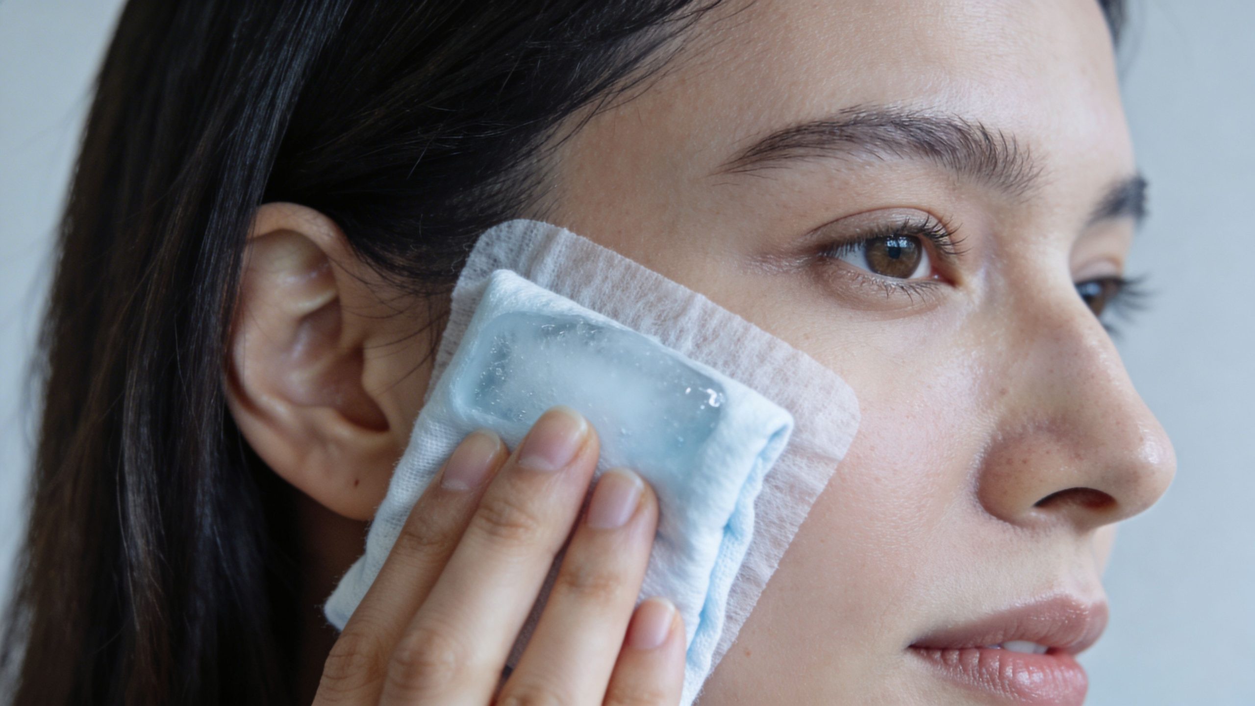 A young woman applying a cold ice pack to her cheek to reduce swelling after dental surgery.