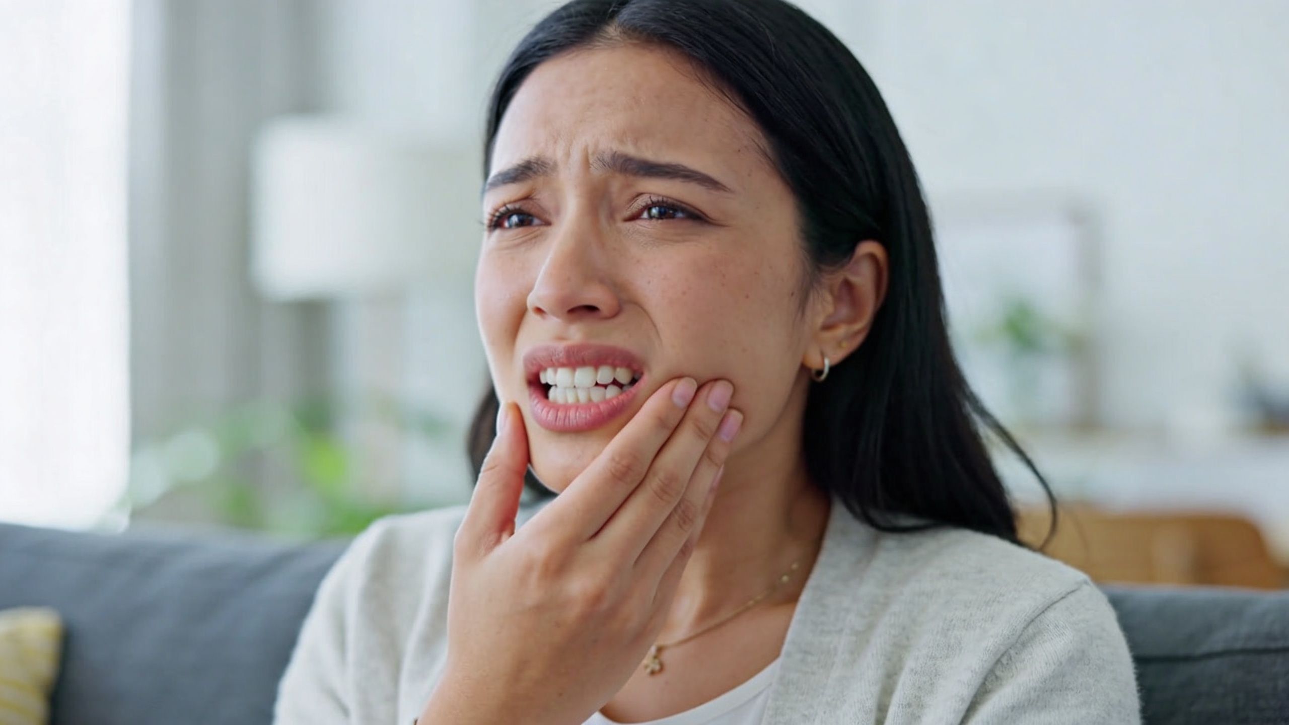 A woman holding her cheek in pain while suffering from a toothache at home.