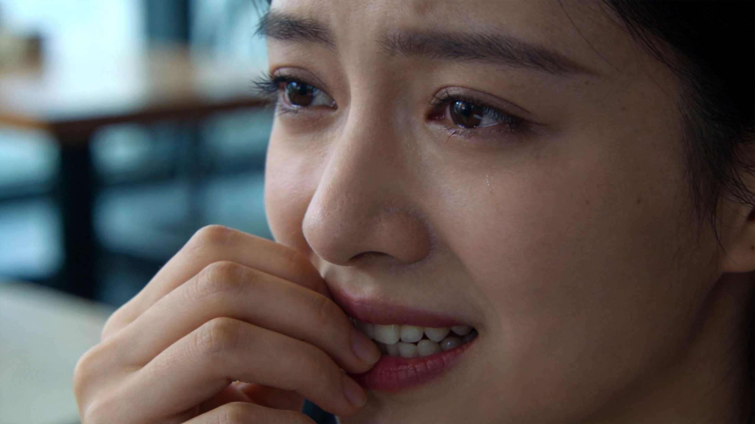 A close-up shot of a young woman crying with her hand near her mouth in distress.