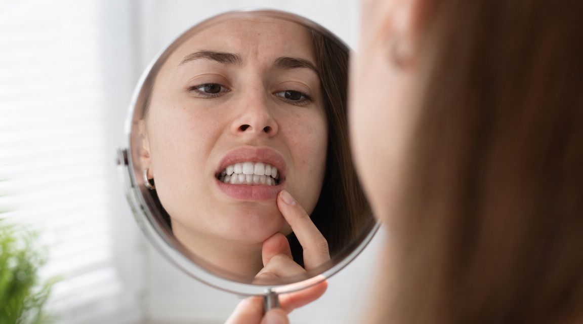 A woman looks at her reflection in a round mirror while examining her very white teeth.