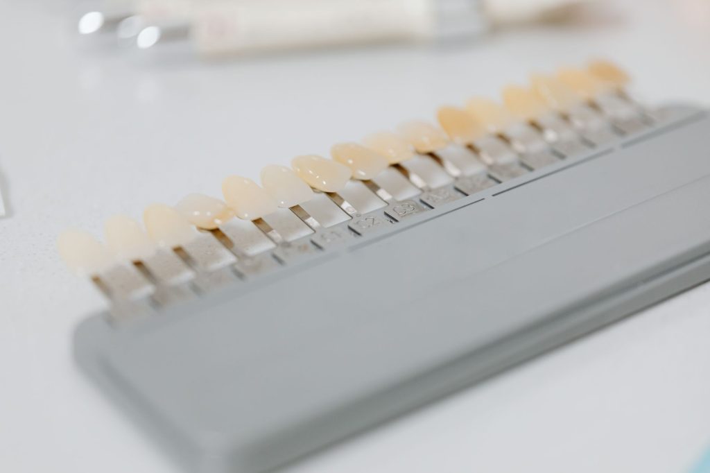 A dental shade guide with a row of tooth-coloured tabs on a white bench, used to compare tooth shades.